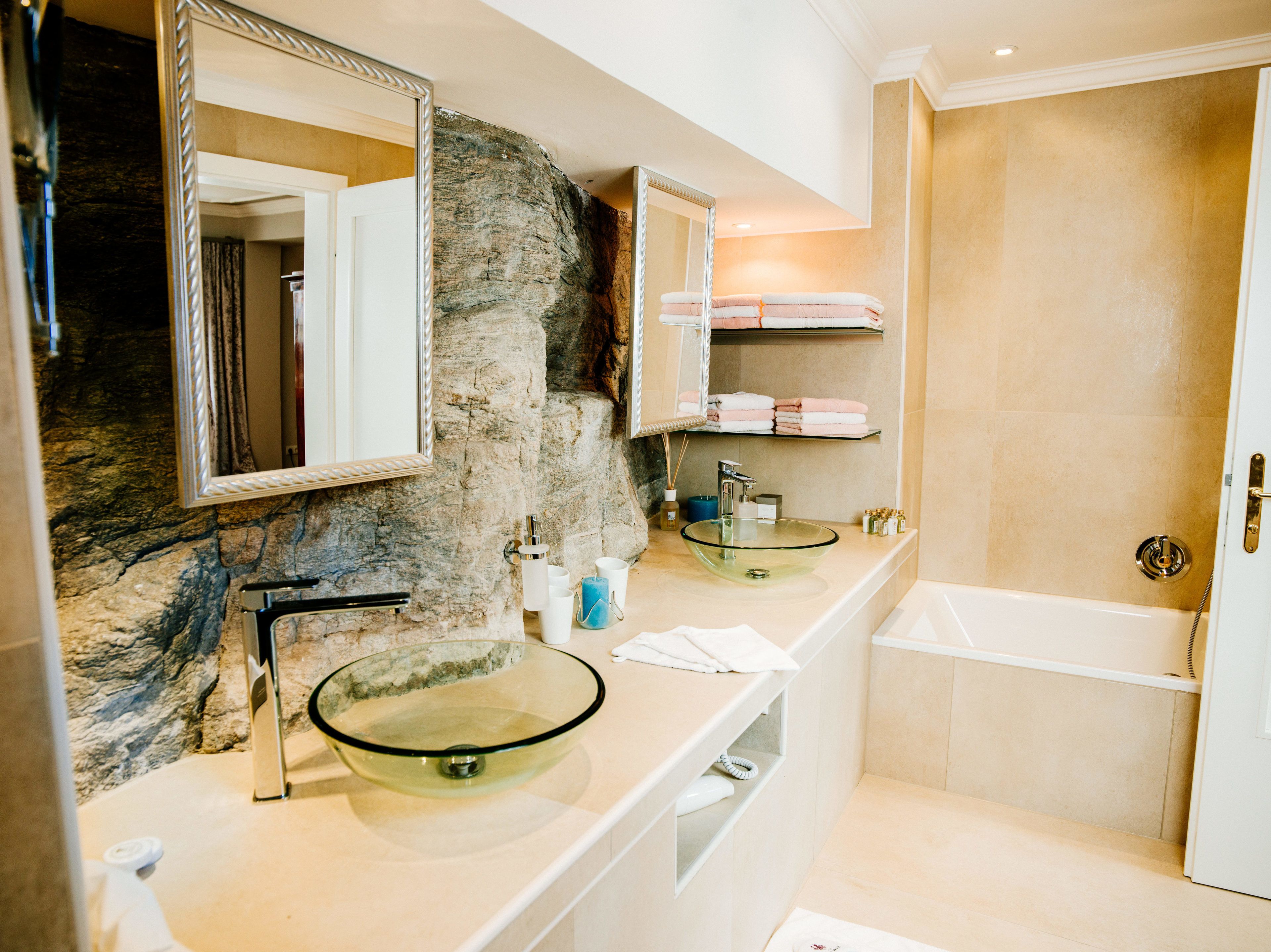 A modern bathroom with a glass sink, a stone accent wall, and a built-in shelf with towels.
