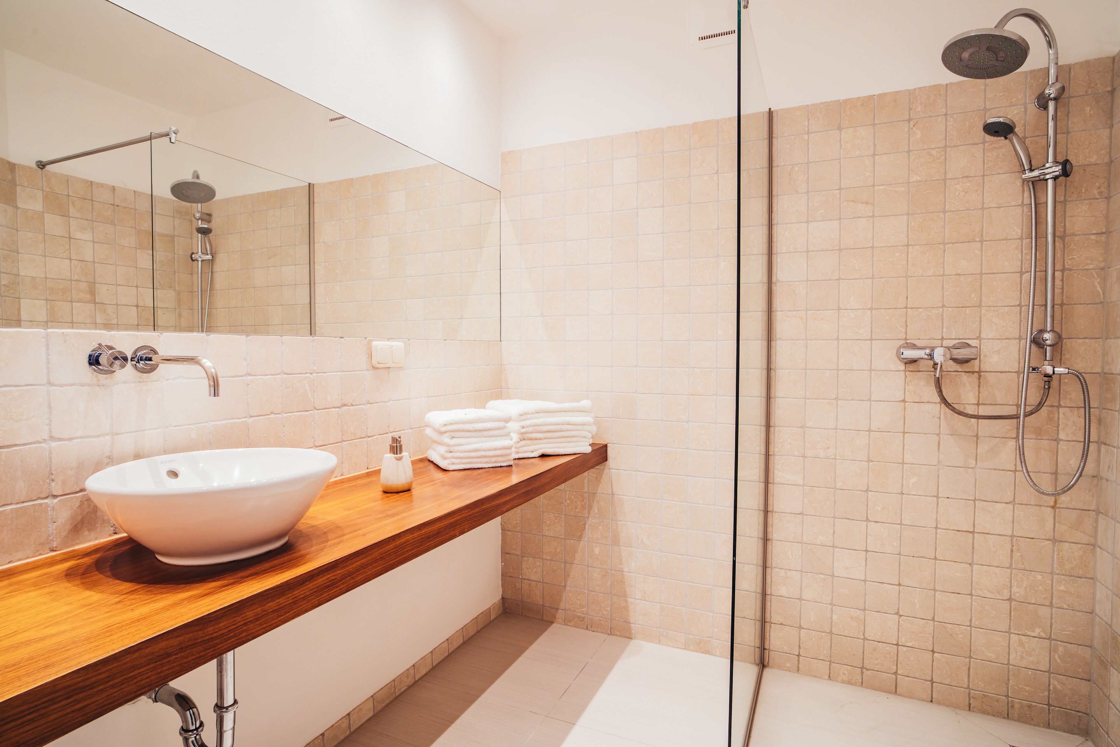 Ein modernes Badezimmer mit einem großen Spiegel, einem Aufsatzwaschbecken, einer Dusche mit Duschbrause und ordentlich gestapelten Handtüchern.