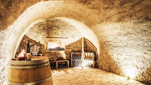 Una bodega subterránea con barriles de madera, estanterías para vino y una vela encendida.