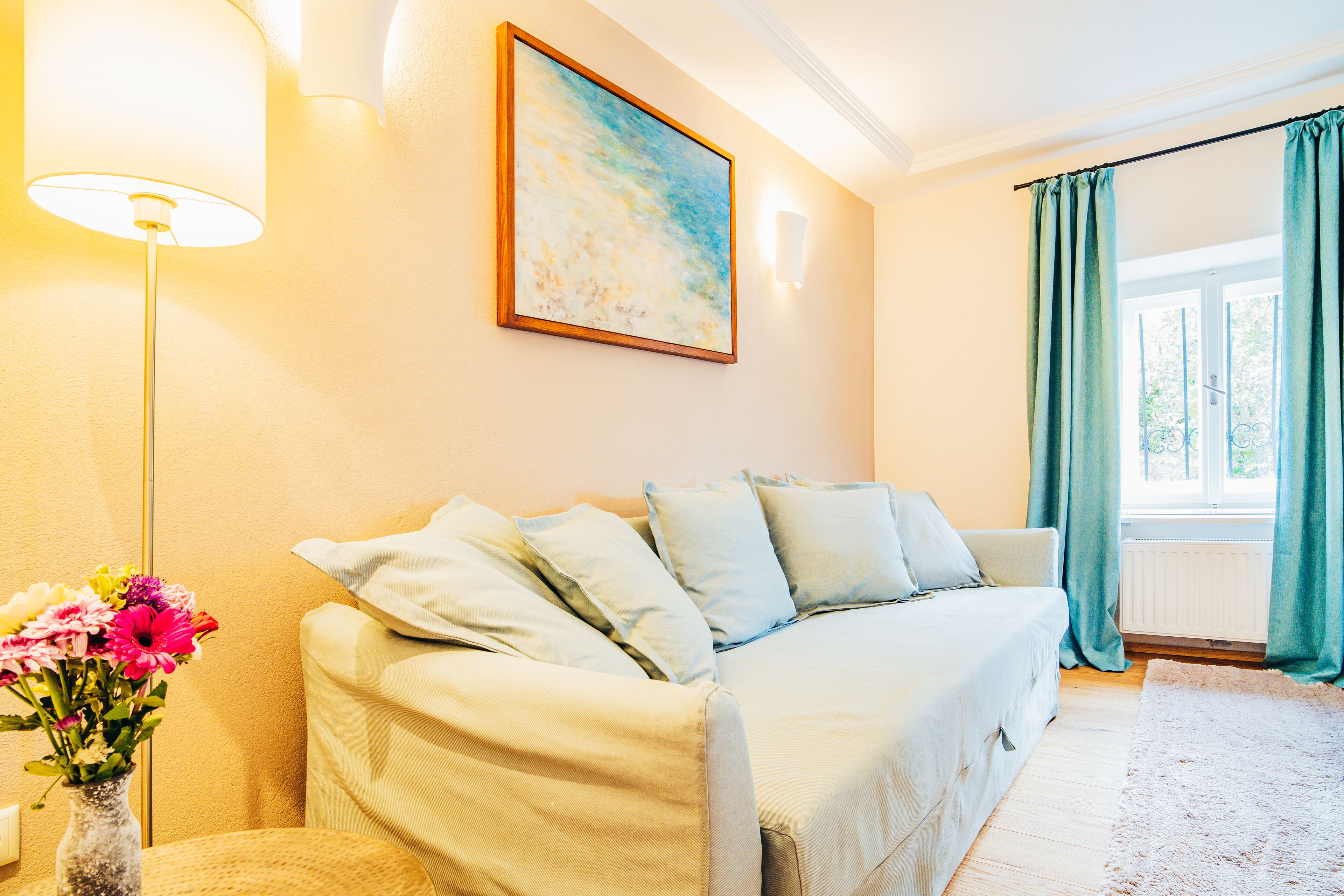 Una habitación acogedora con un sofá, un jarrón de flores y un cuadro en la pared.