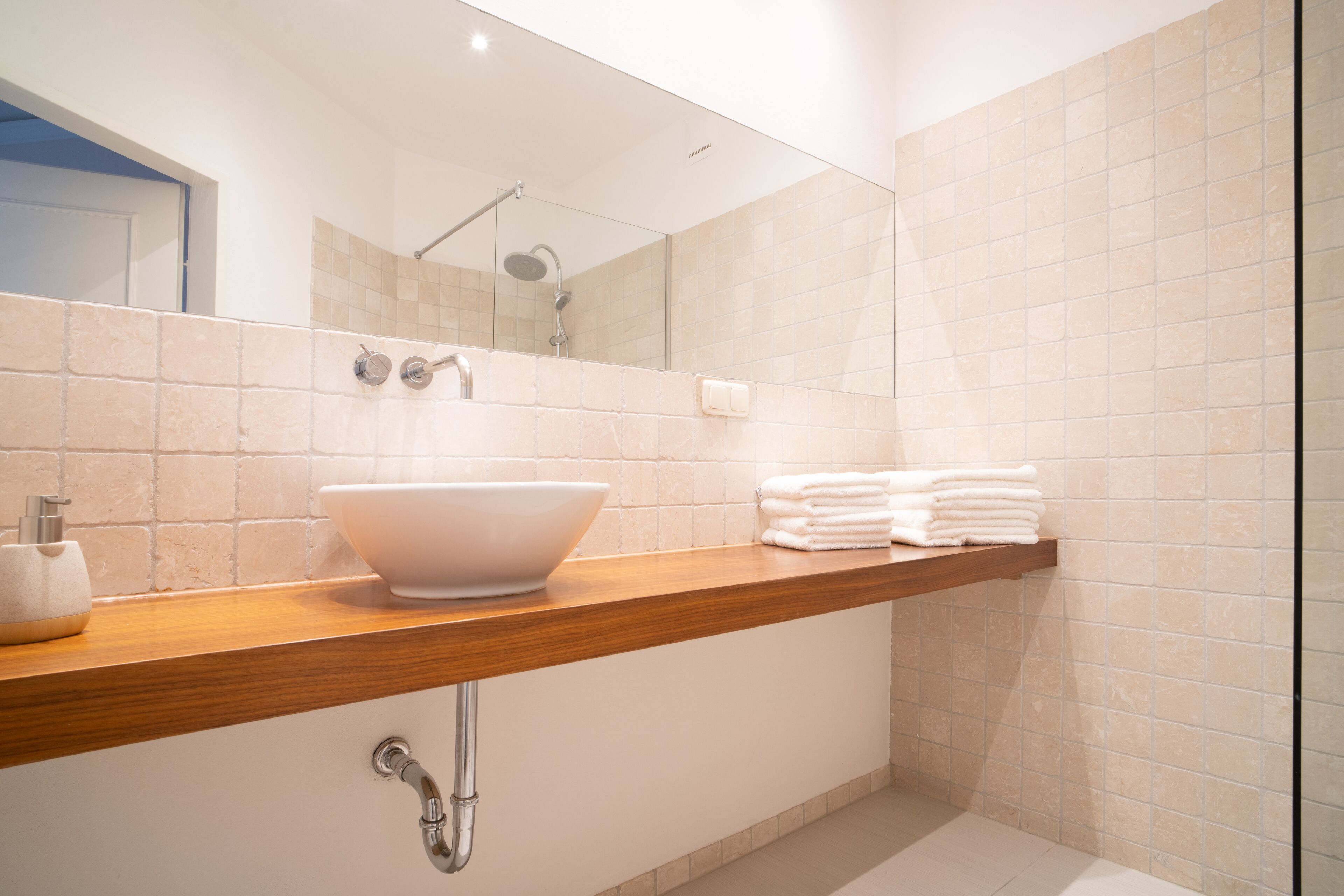 A modern bathroom with a large mirror, a wooden vanity, a white sink, and a shower area.
