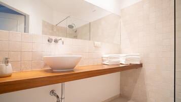 A modern bathroom with a large mirror, a wooden vanity, a white sink, and a shower area.