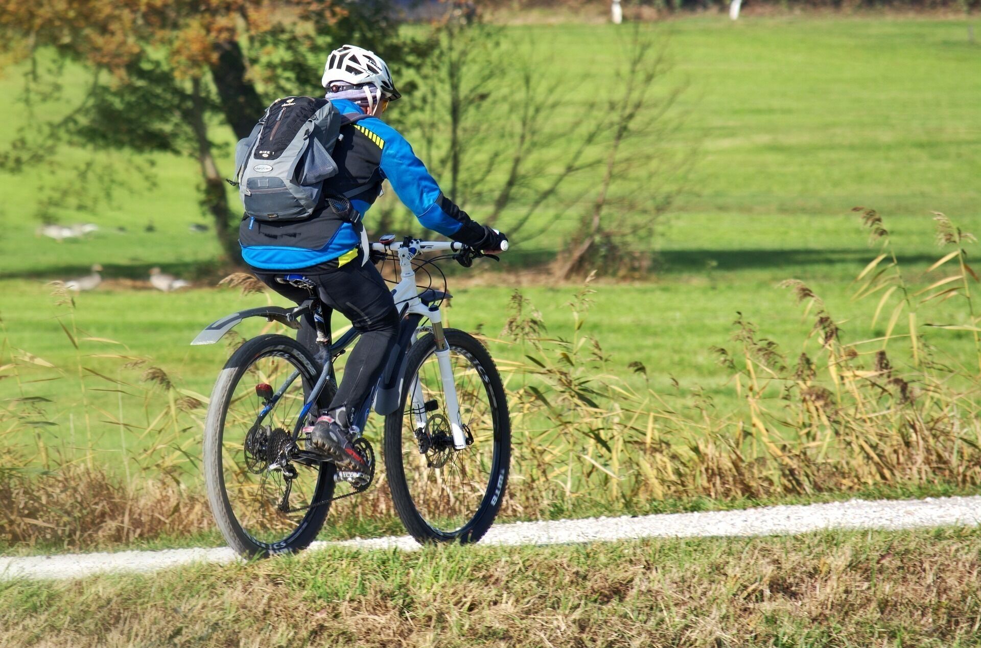 Ein Radfahrer auf einem Rennrad in ländlicher Umgebung, mit einem grasbewachsen Feld und Bäumen im Hintergrund.