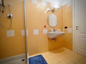 Een badkamer met gele tegels, een witte wastafel, een spiegel en een douche.