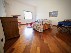 Een kamer met een bed, een houten bureau, een rode bank, een tafel met een blauwe tafelkleed en een schilderij aan de muur.