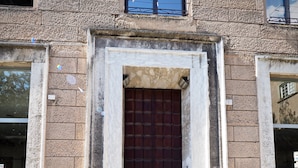 Facciata di un edificio con un'ampia porta in legno scuro, muri in pietra e una piccola finestra sopra la porta.