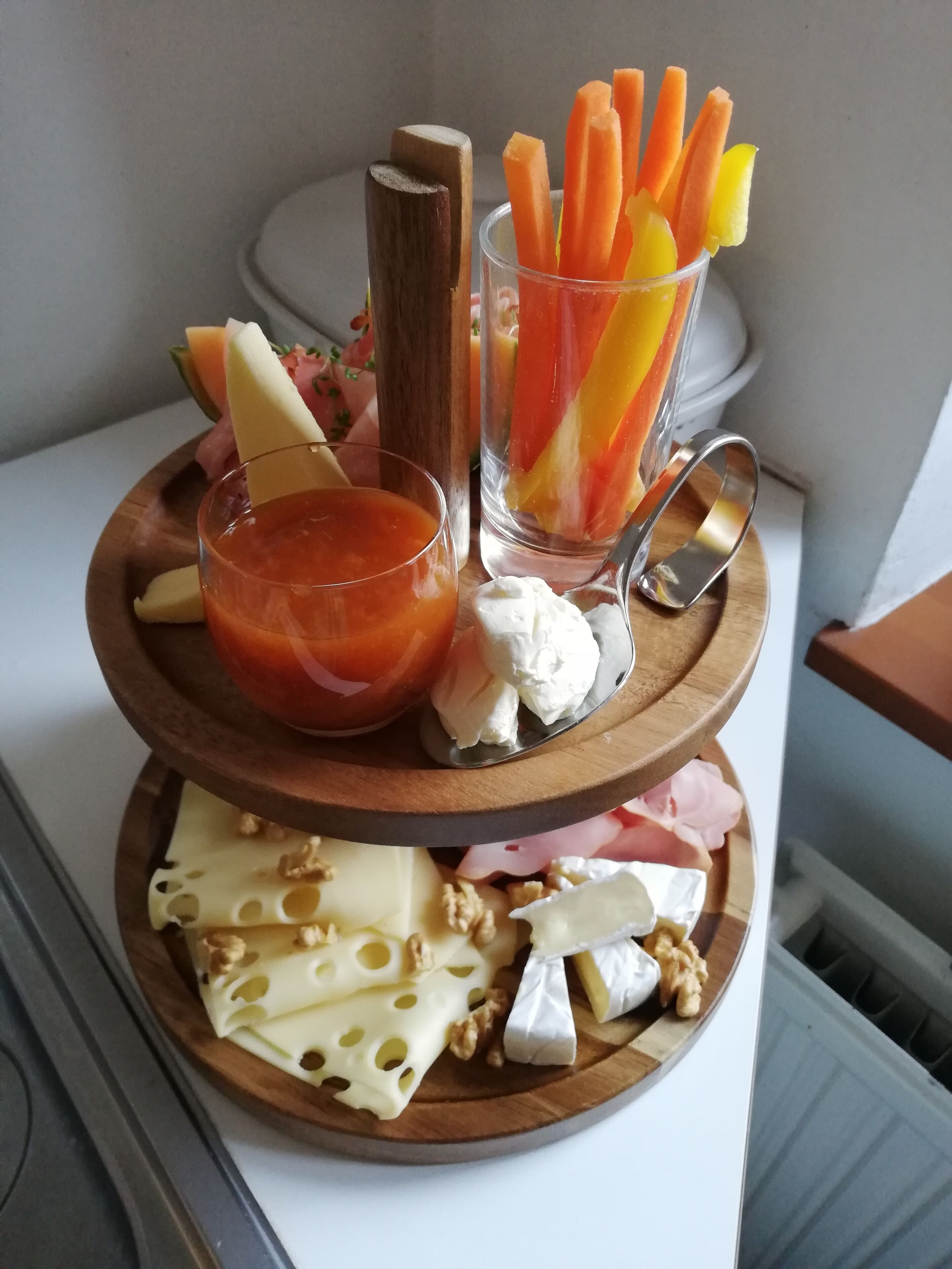A wooden serving tray with various cheeses, fruits, and a glass of juice.