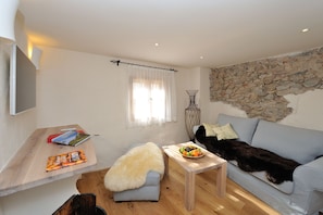Una sala de estar acogedora con una pared de piedra, un sofá azul claro, una mesa de centro de madera con un frutero, un plaid suave sobre un sofá azul y un televisor montado.