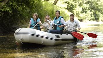 A group of people in a white inflatable raft on a calm river surrounded by dense greenery.