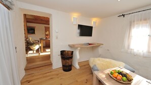A room with a wooden floor, a white wall, a mounted TV, a small table with a fruit bowl, and a fur throw on a bench. - Heritage Dürnstein (Durnstein)