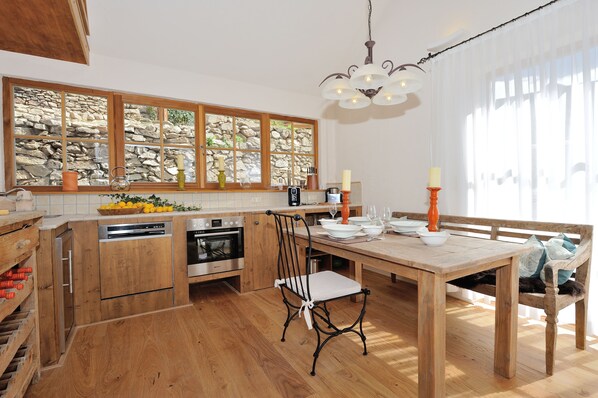 Una cocina con armarios de madera, una pared de piedra, una mesa de comedor con sillas y una lámpara de araña.