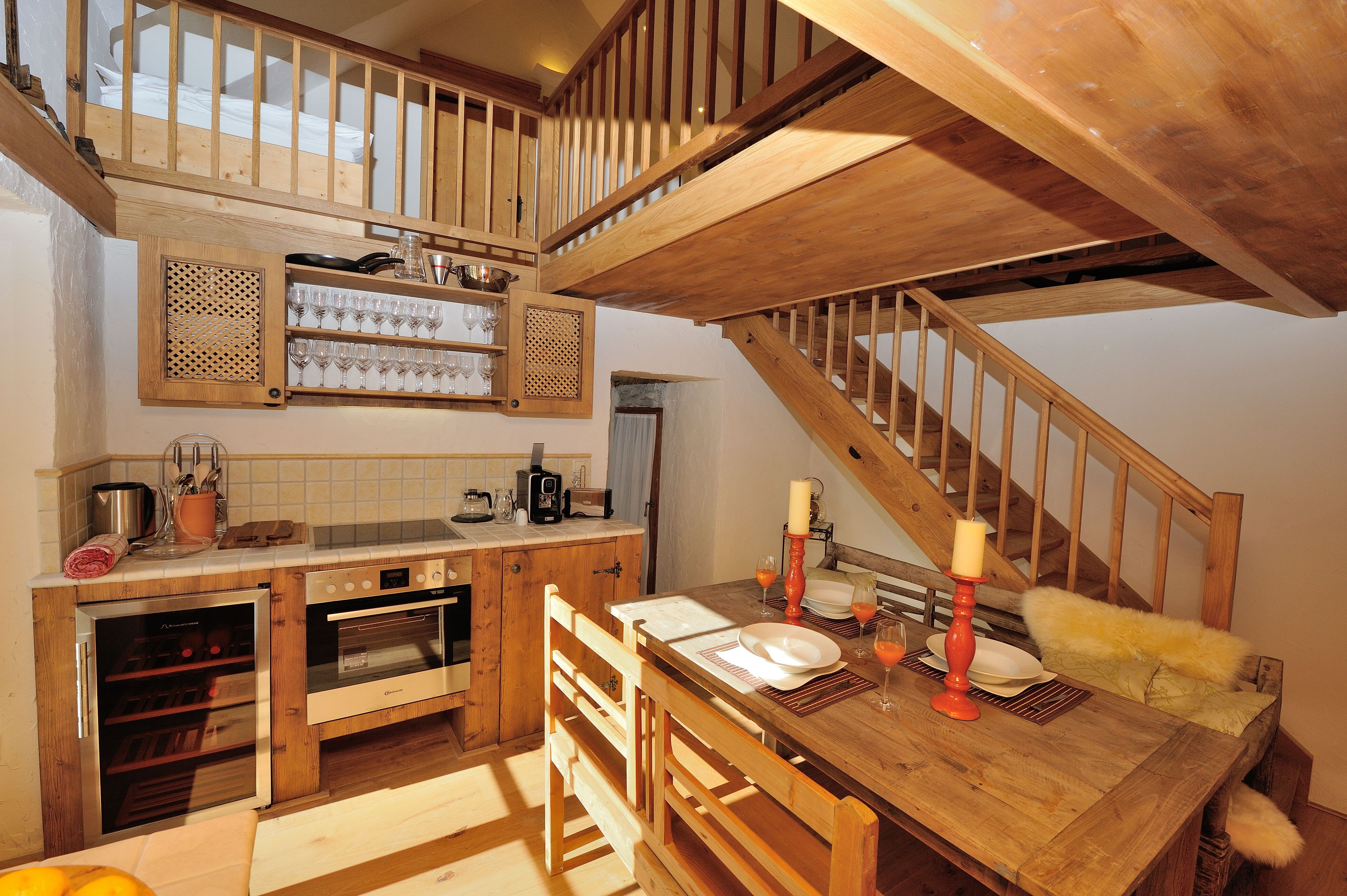 A kitchen with wooden cabinetry, a dining table set with plates and glasses, and a staircase with wooden railings.