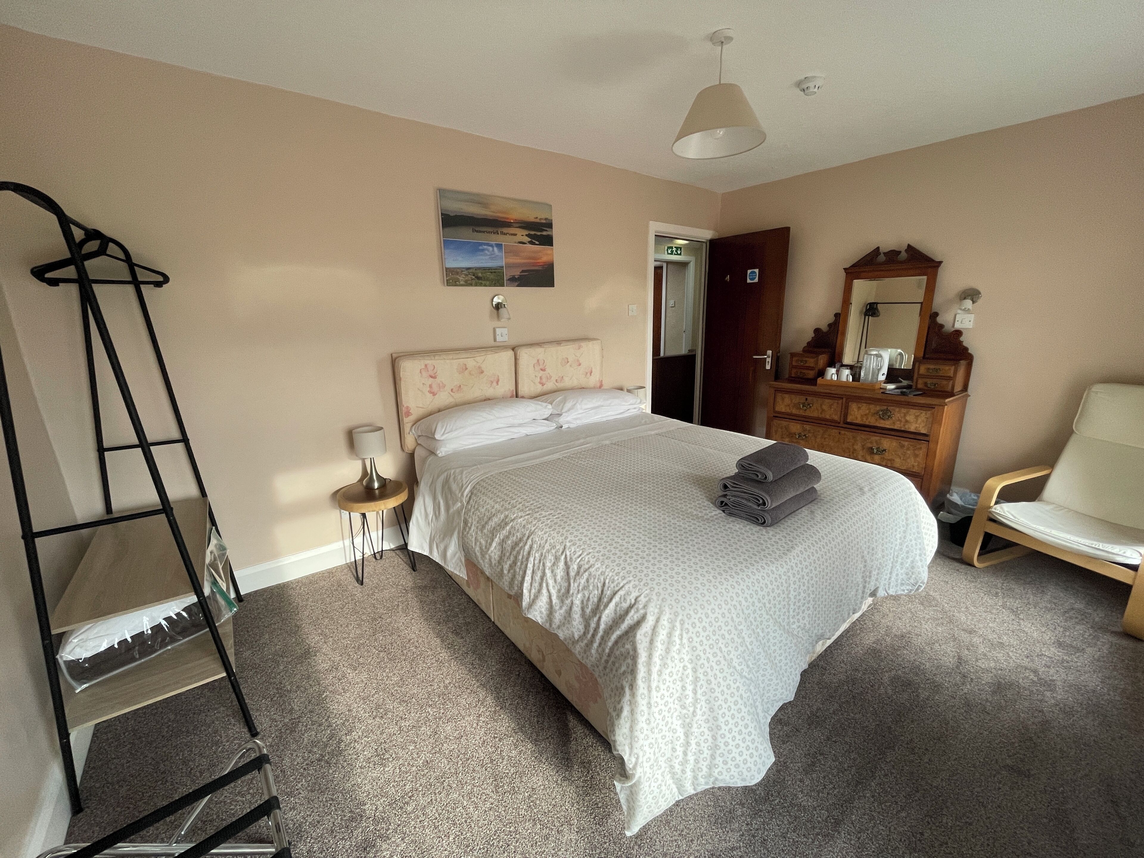 A bedroom with a bed, a dresser, a chair, a ladder, and a painting on the wall.