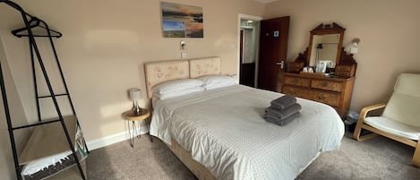 A bedroom with a bed, a dresser, a chair, a ladder, and a painting on the wall.