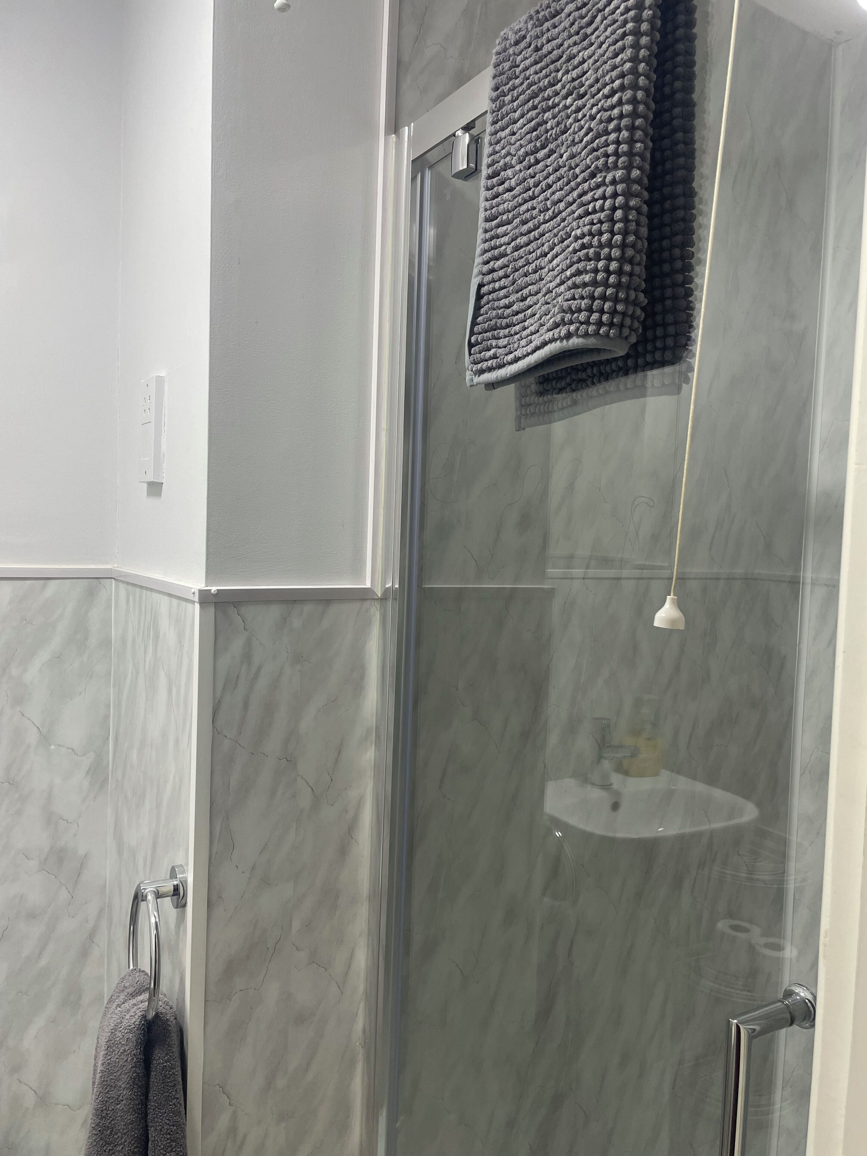 Een moderne badkamer met een douchecabine van glas, een handdoekhouder en een marmeren wand.