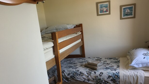 A single bed with a wooden frame, a floral bedspread, and a white pillow. There is a small wooden stool and a framed picture on the wall. - Carnside Guest House (Bushmills)