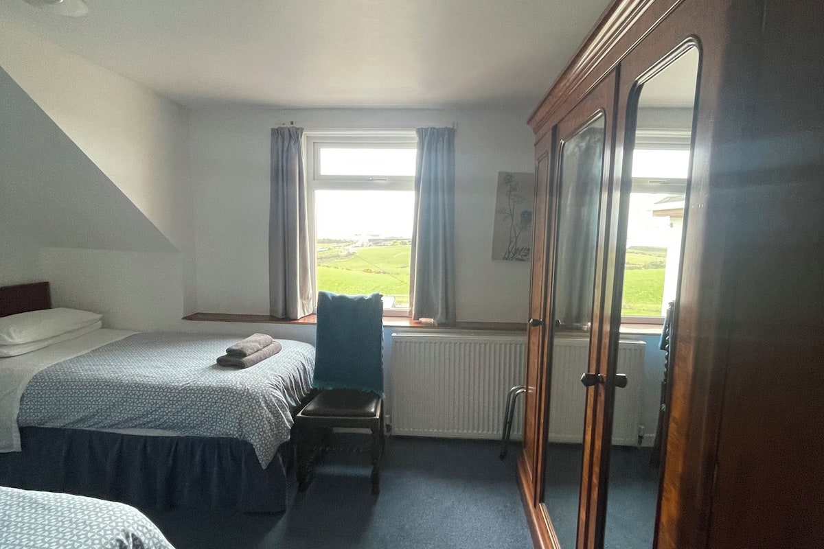 Un dormitorio con dos camas, una silla, un armario y una ventana con cortinas.