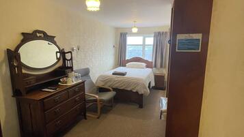 Hotelkamer met een bed, een kaptafel, een spiegel, een bureau, een stoel, een raam met gordijnen en een deur met een bordje.