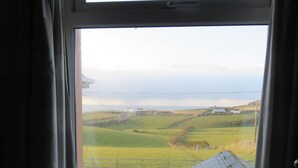 A window with a view of a green landscape and a building in the distance. - Carnside Guest House (Bushmills)