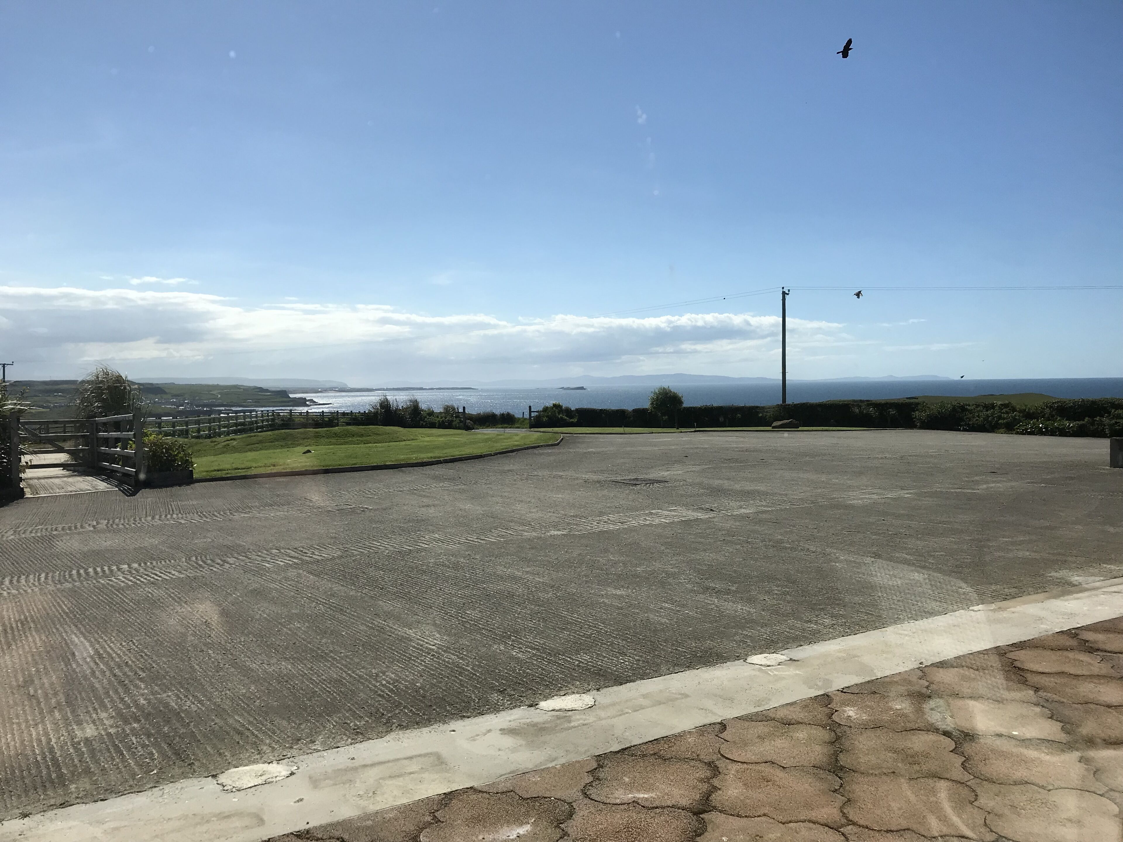 Uma área de estacionamento pavimentada com vista para o mar e colinas ao longe.