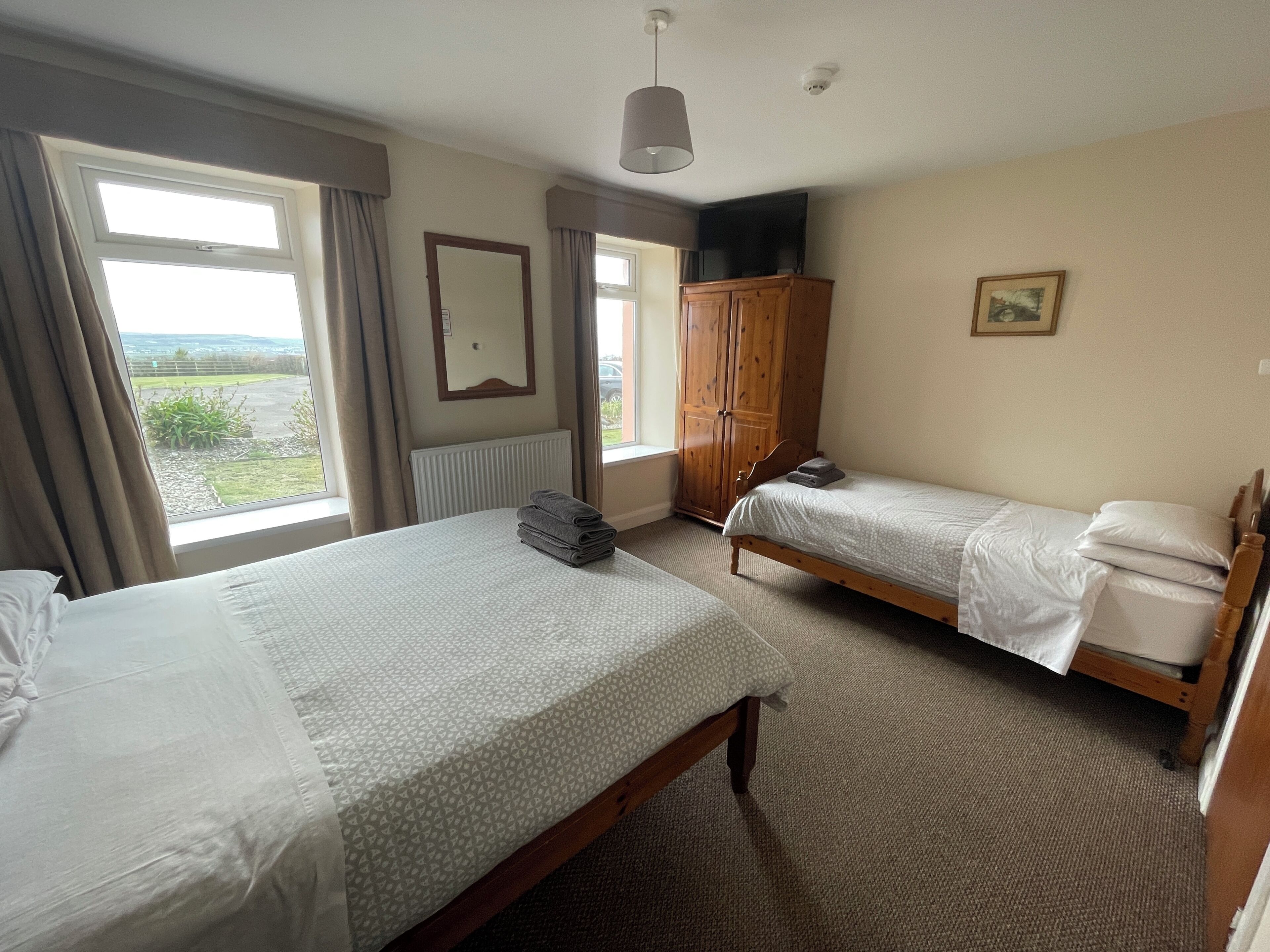 A hotel room with two beds, a wardrobe, a mirror, and a view of the outdoors.