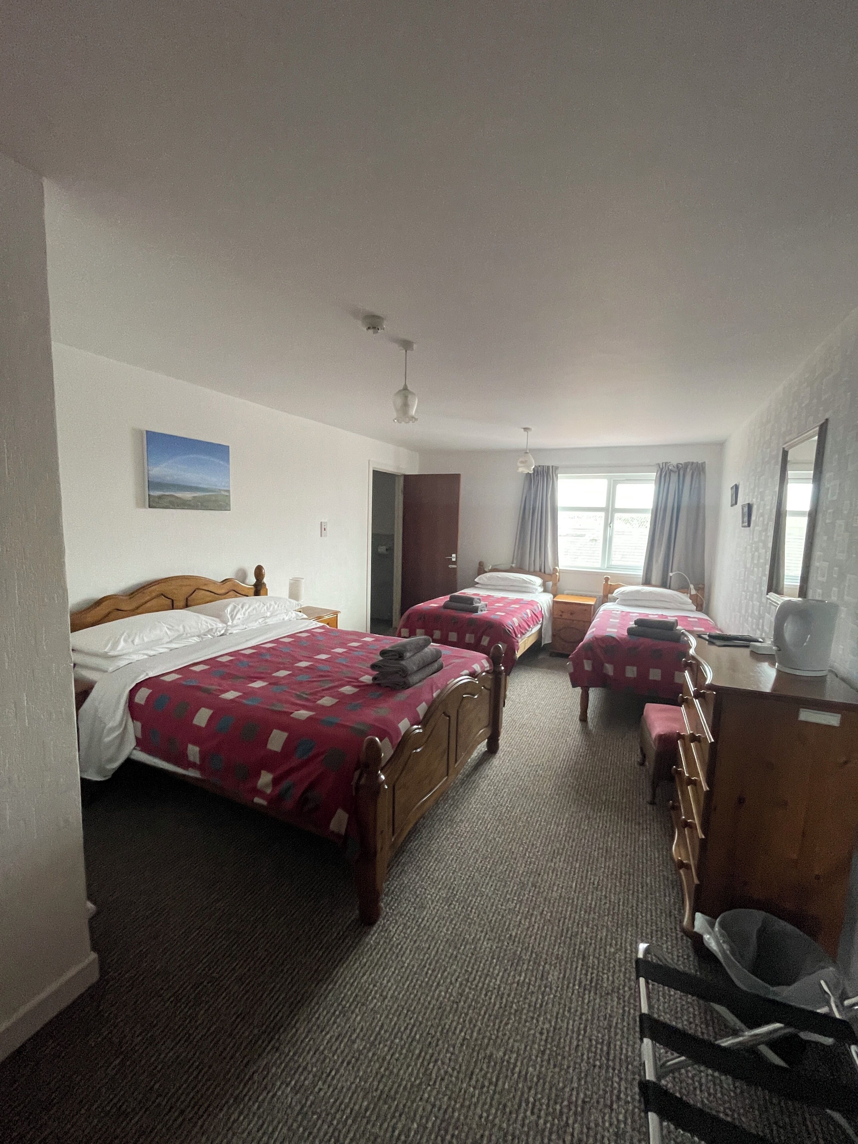 Ein Hotelzimmer mit zwei Betten, einem Schreibtisch, einem Stuhl, einem Kleiderschrank und einem Fenster mit Vorhängen.