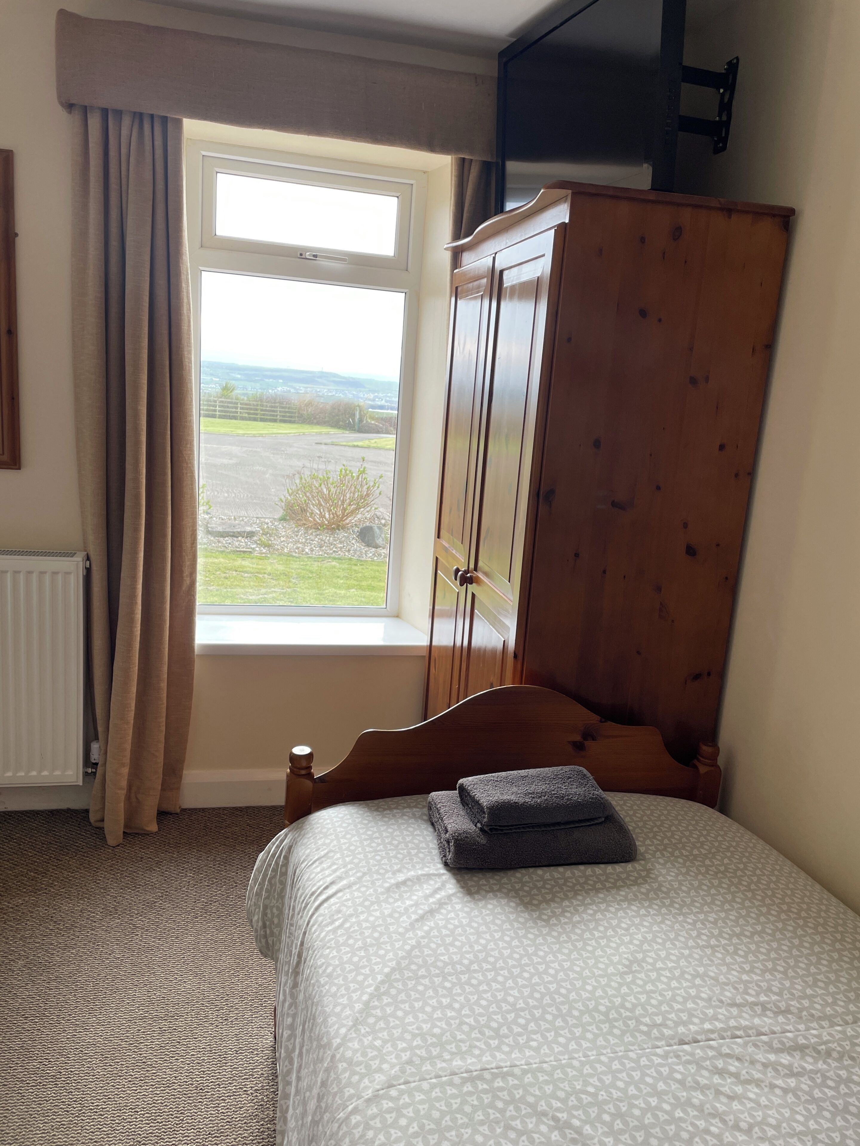A bedroom with a bed, a window with curtains, a radiator, and a wooden wardrobe.