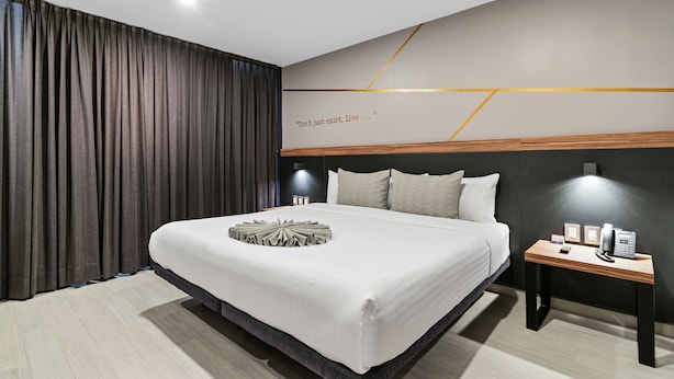 Habitación de hotel moderna con una cama grande, una mesita de noche con lámpara y una pared con una cita motivacional.