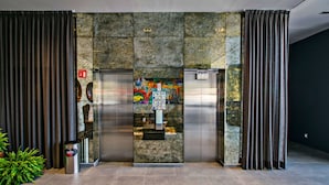 Un ascensor con panel de control e instrucciones de emergencia, flanqueado por cortinas y una pared de piedra.