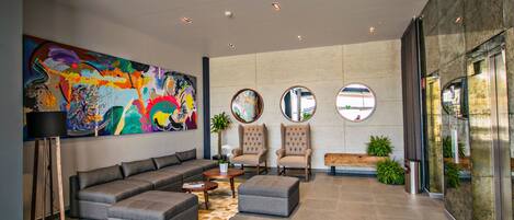 A modern lobby with a sectional sofa, two armchairs, a coffee table, and a large abstract painting.