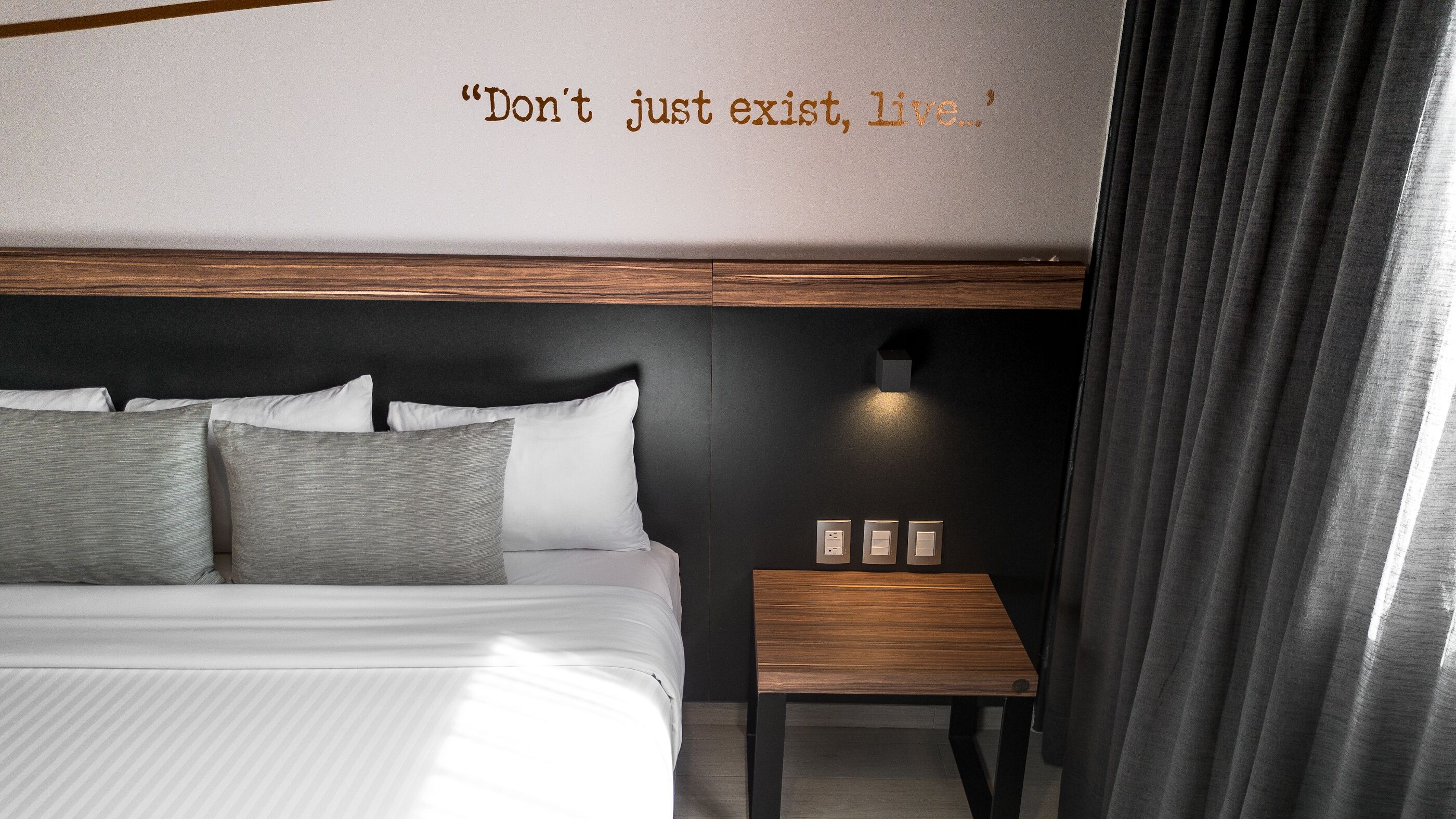 Una habitación de hotel moderna con una cama grande, una mesita de noche y una lámpara de pared.