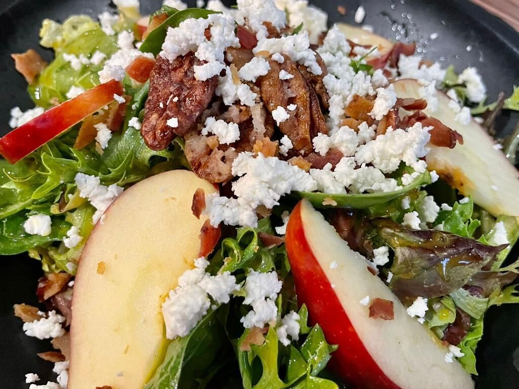 A salad with greens, apples, and crumbled cheese.