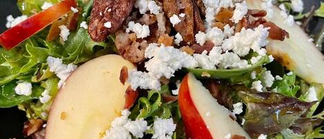 A salad with greens, apples, and crumbled cheese.