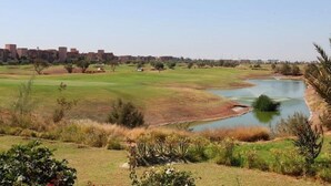 A golf course with a pond, surrounded by buildings and sparse vegetation. - Villa Firdaous (Marrakech)