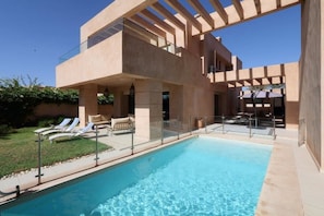 Una piscina al aire libre, sombrillas, sillones reclinables de piscina