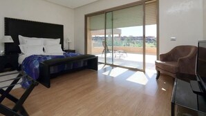 A bedroom with a bed, a bench, a TV, and a balcony with a chair. - Villa Firdaous (Marrakech)