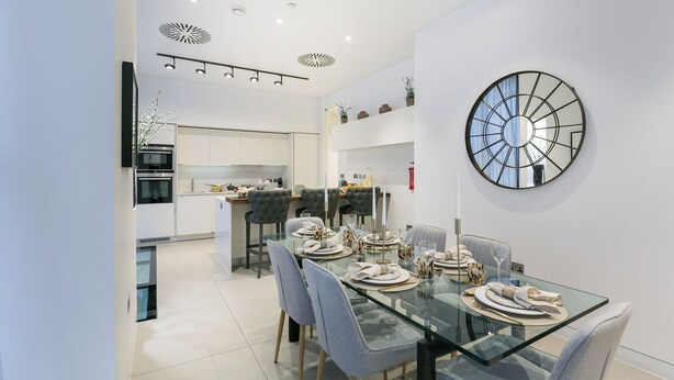 Un comedor moderno con una mesa de vidrio, sillas grises y un reloj de pared decorativo.