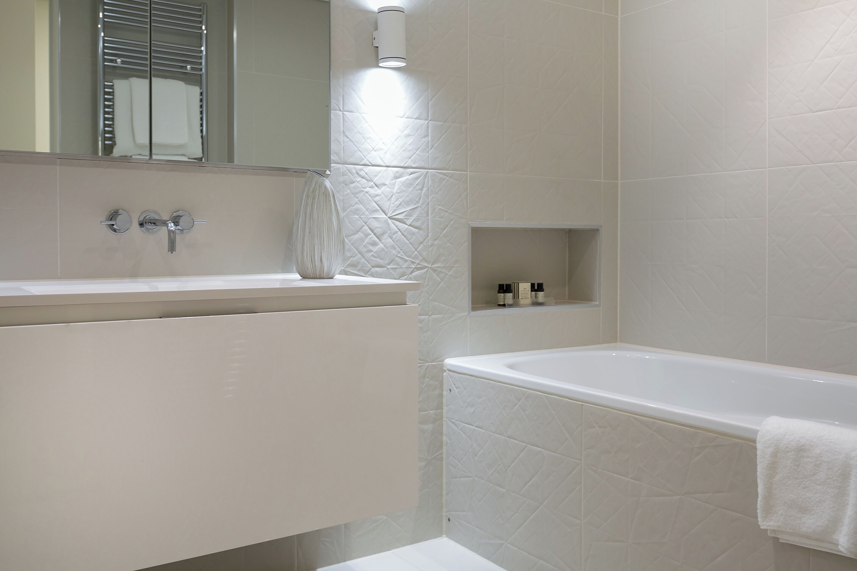 Une salle de bain moderne avec un meuble-lavabo blanc, une baignoire et une petite étagère contenant des articles de toilette.