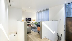 Una sala moderna con sofá, mesa de centro y televisor. Se ve una escalera que lleva a otro nivel.