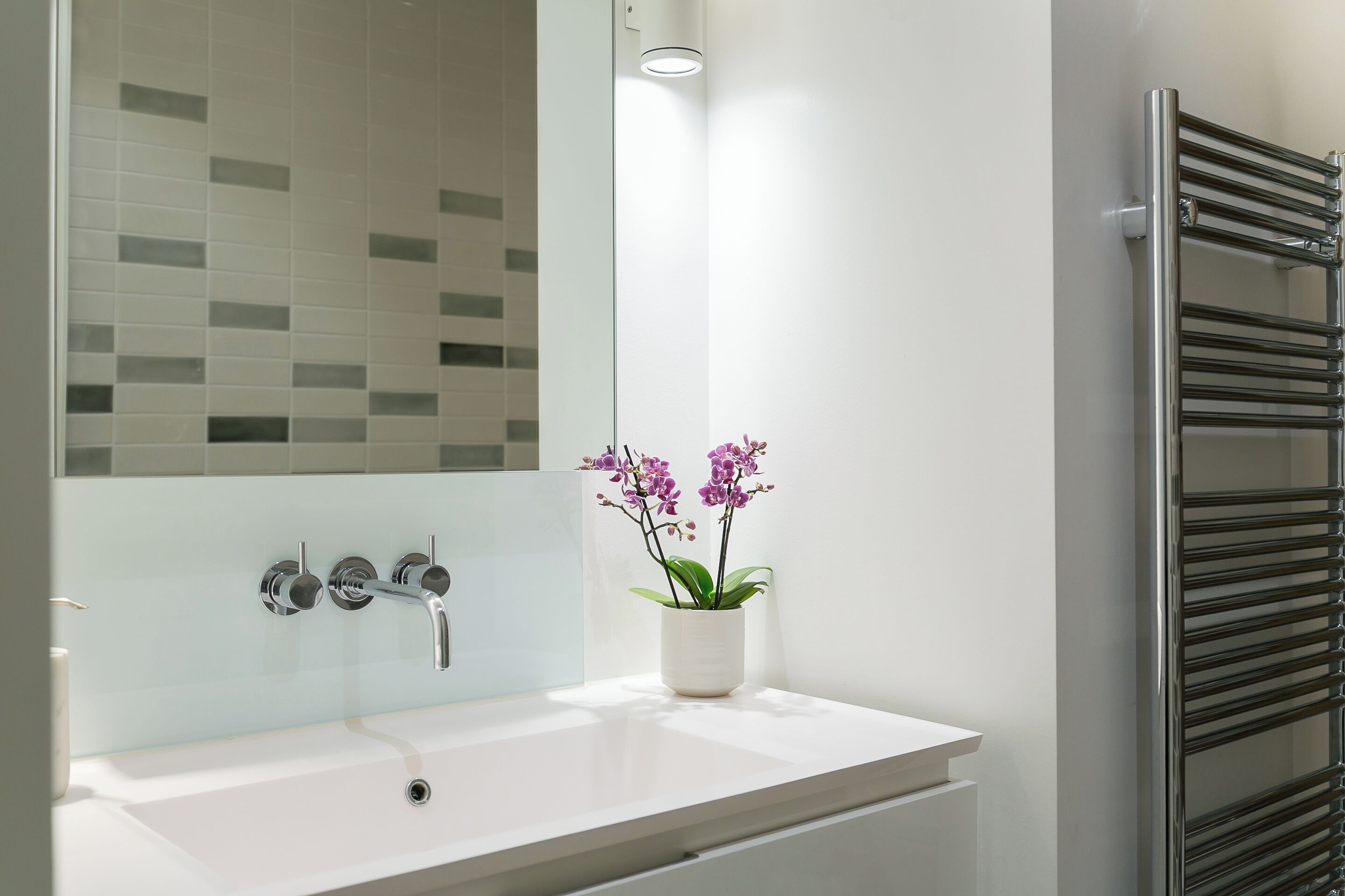 Une salle de bain moderne avec un lavabo blanc, deux robinets, un miroir et une orchidée en pot.