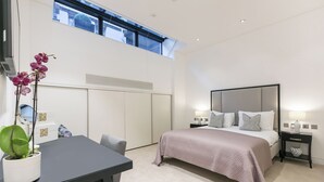 Un dormitorio moderno con una cama grande, un escritorio y una orquídea en maceta.