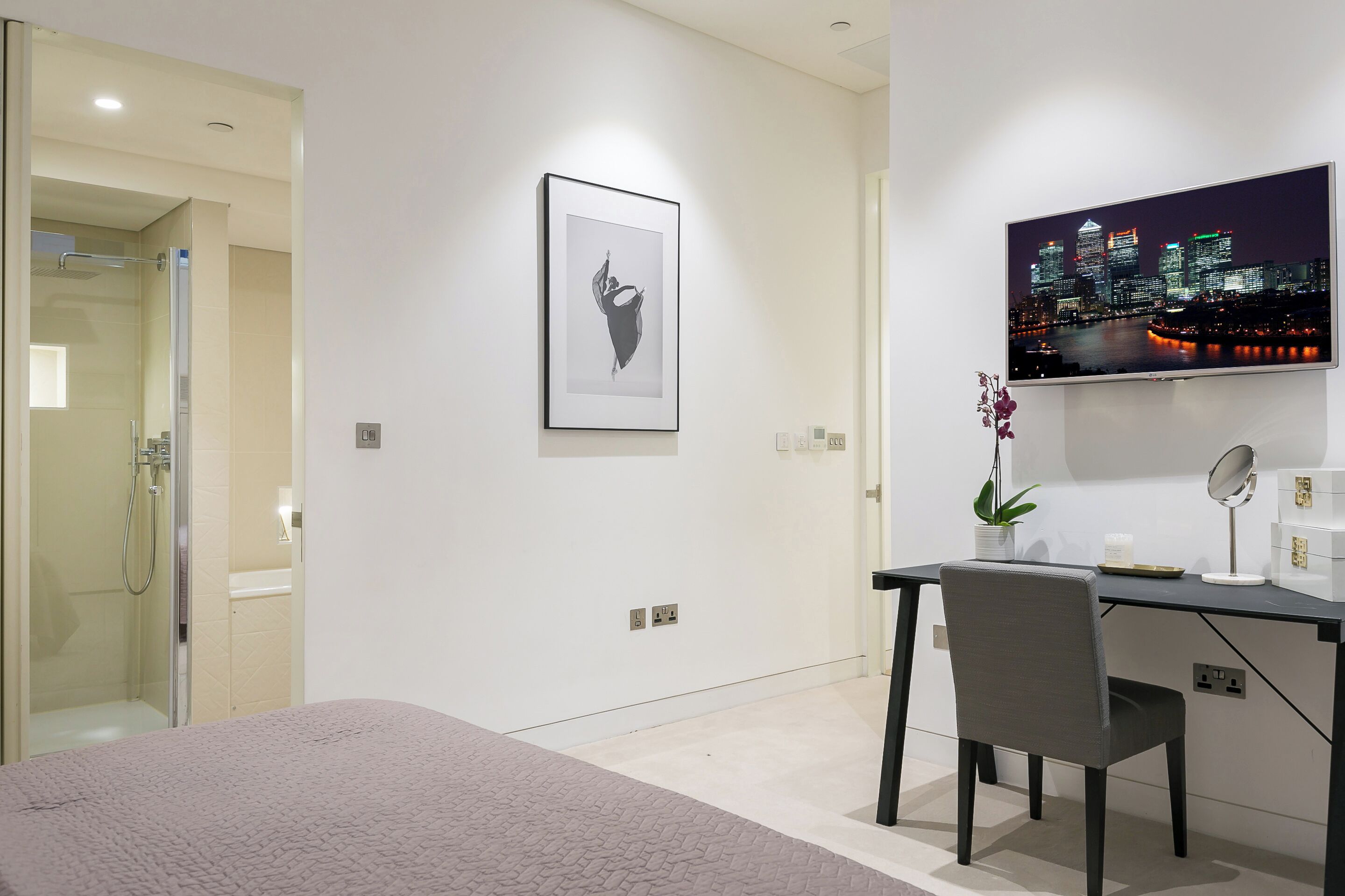 Camera d'albergo moderna con un letto, una scrivania con una sedia, una doccia, un quadro incorniciato e una televisione con vista sulla città.
