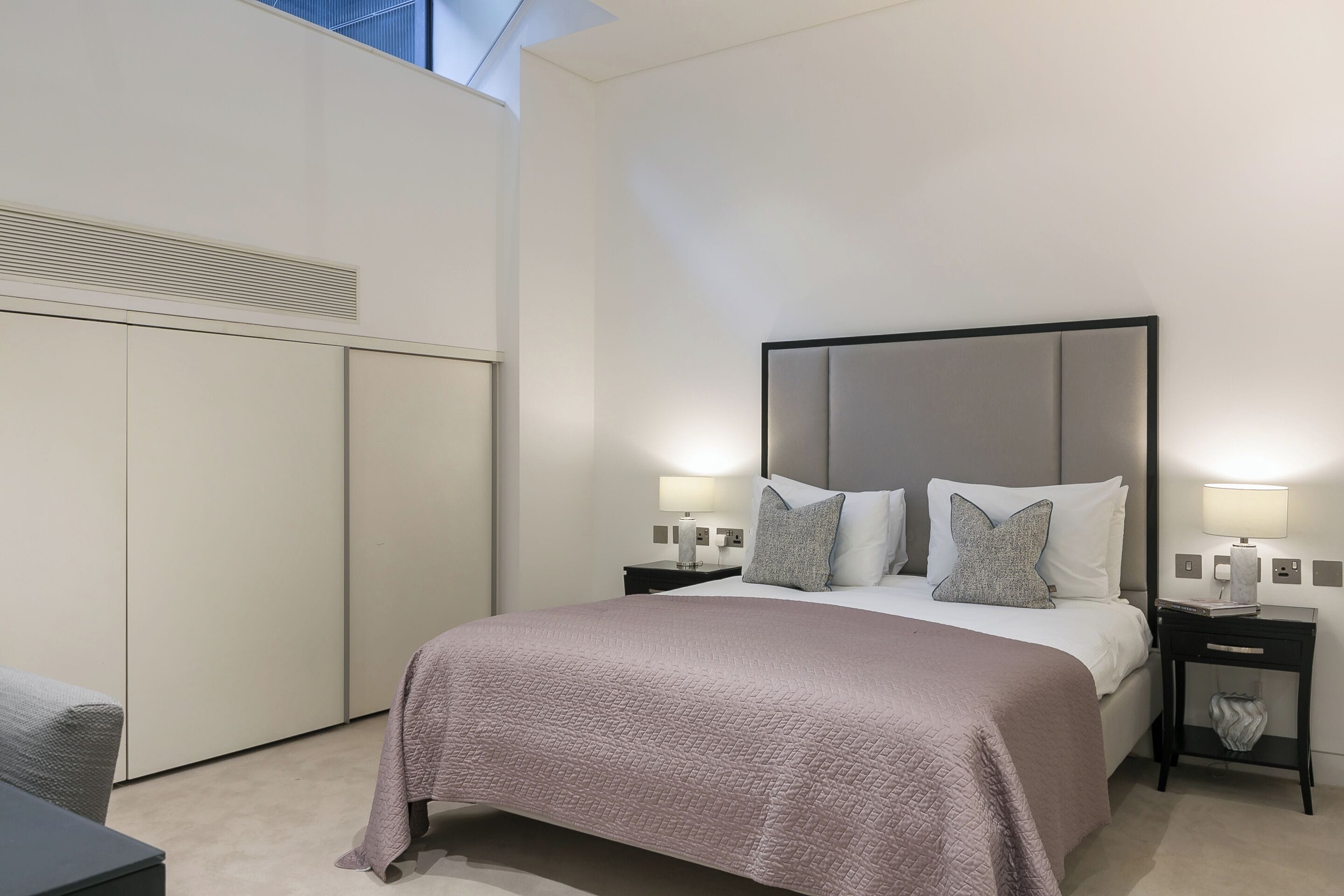 Ein modernes Hotelzimmer mit einem großen Bett, zwei Nachttischen mit Lampen, einem Kleiderschrank und Blick auf den Himmel.