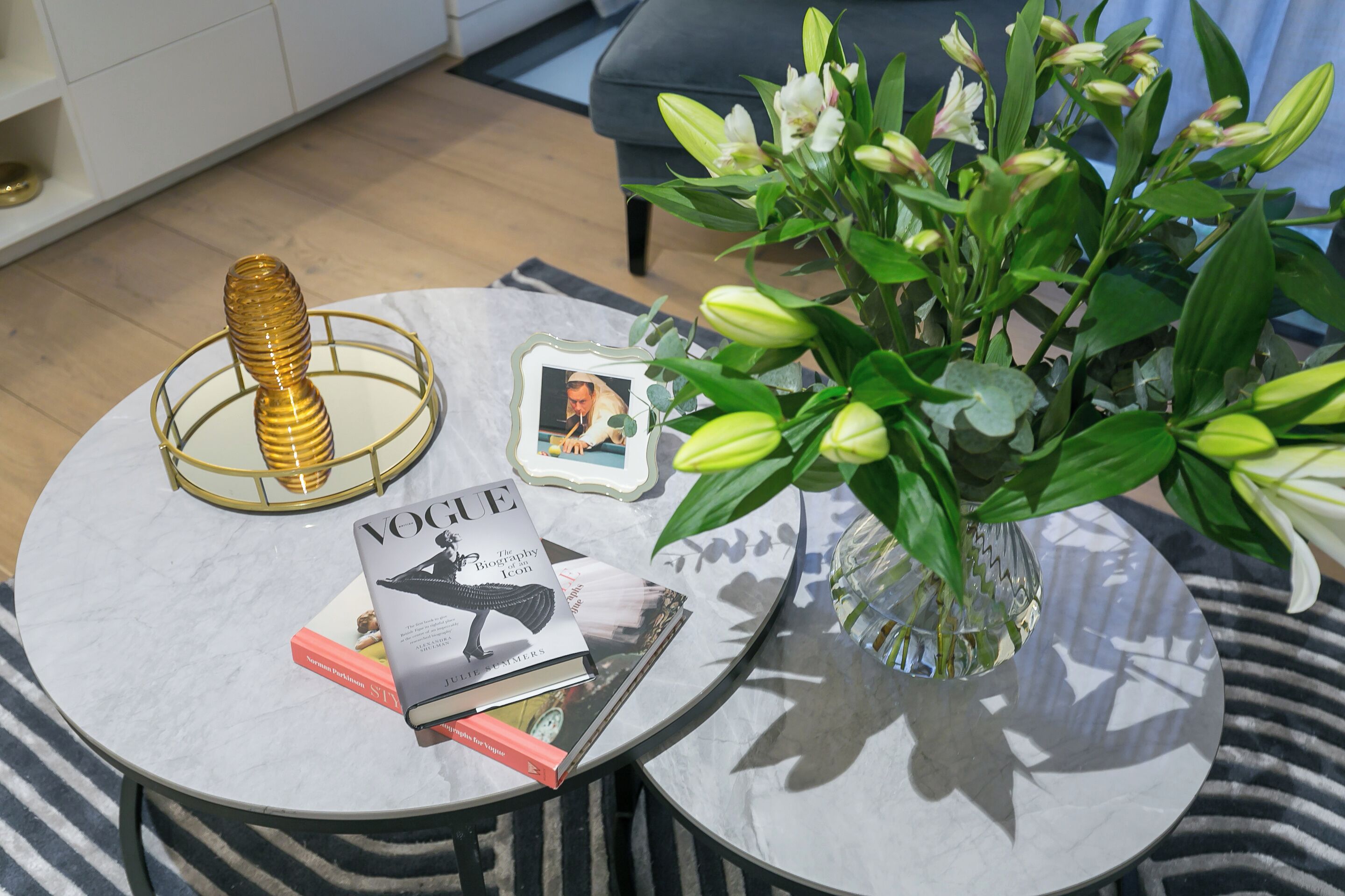 A round table with a magazine, a book, a decorative item, and a vase with flowers.