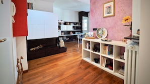 A modern living room with a wooden floor, white furniture, and a pink accent wall. - Lussuosa Dimora Fiumara (Genoa)