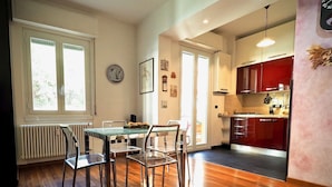 A spacious dining area with a glass table and chairs, a kitchen with red cabinets, and a large window providing natural light. - Lussuosa Dimora Fiumara (Genoa)