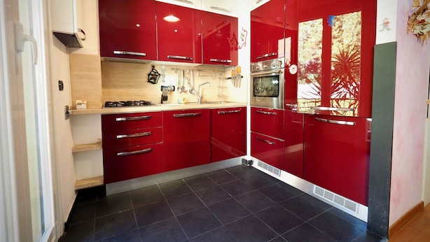 A modern kitchen with red cabinets, stainless steel appliances, and a tiled floor. - Lussuosa Dimora Fiumara (Genoa)