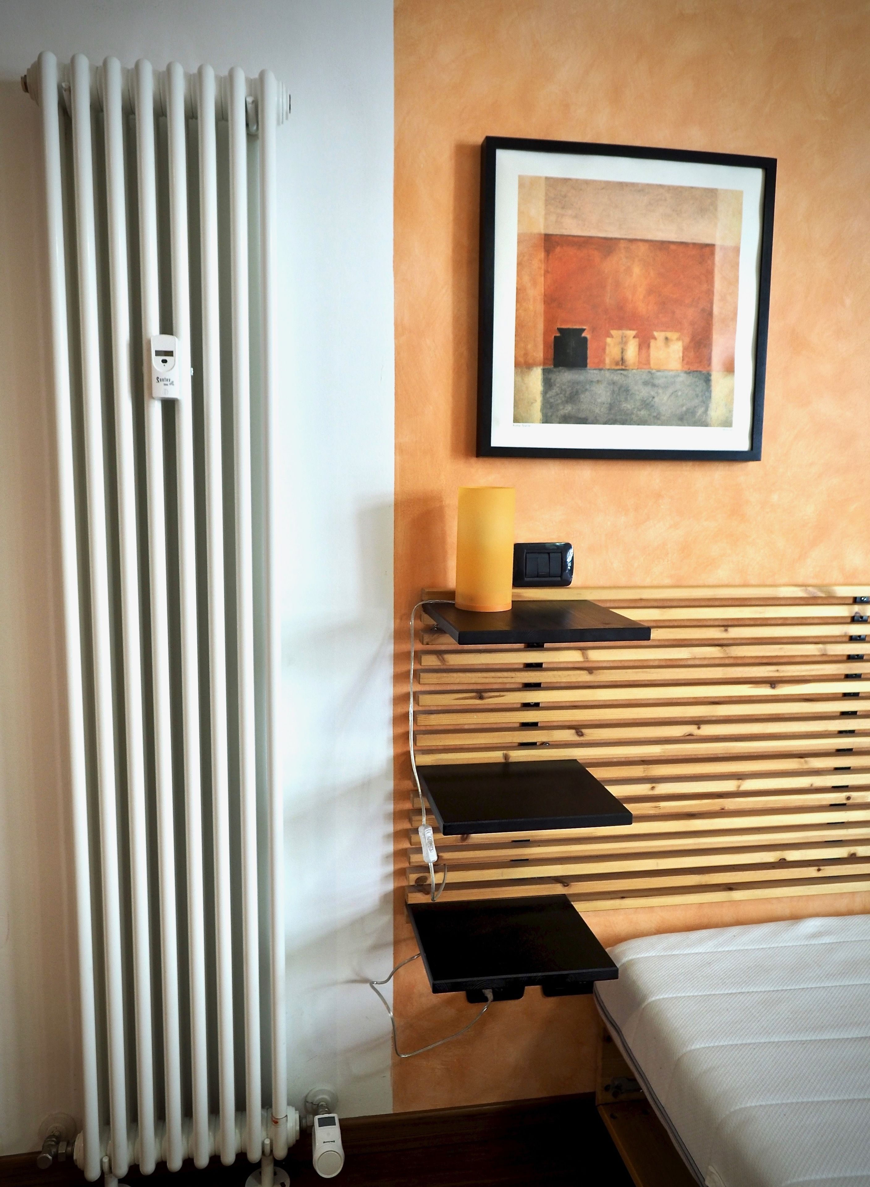 Une pièce avec un radiateur, un tableau encadré, une bougie et un lit.