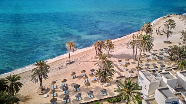 A beach with palm trees, sun loungers, and umbrellas. - Hari Club Beach Resort (Aghir)