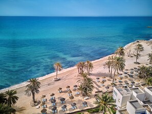 A beach with palm trees, sun loungers, and umbrellas.